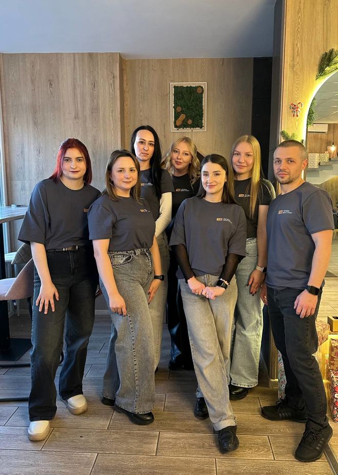 A group of young adults stand together indoors, all wearing matching dark t-shirts and jeans.